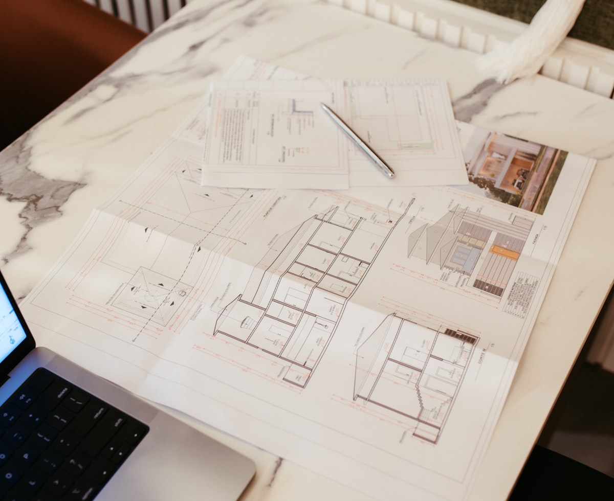 Planos arquitectónicos y una laptop sobre un escritorio